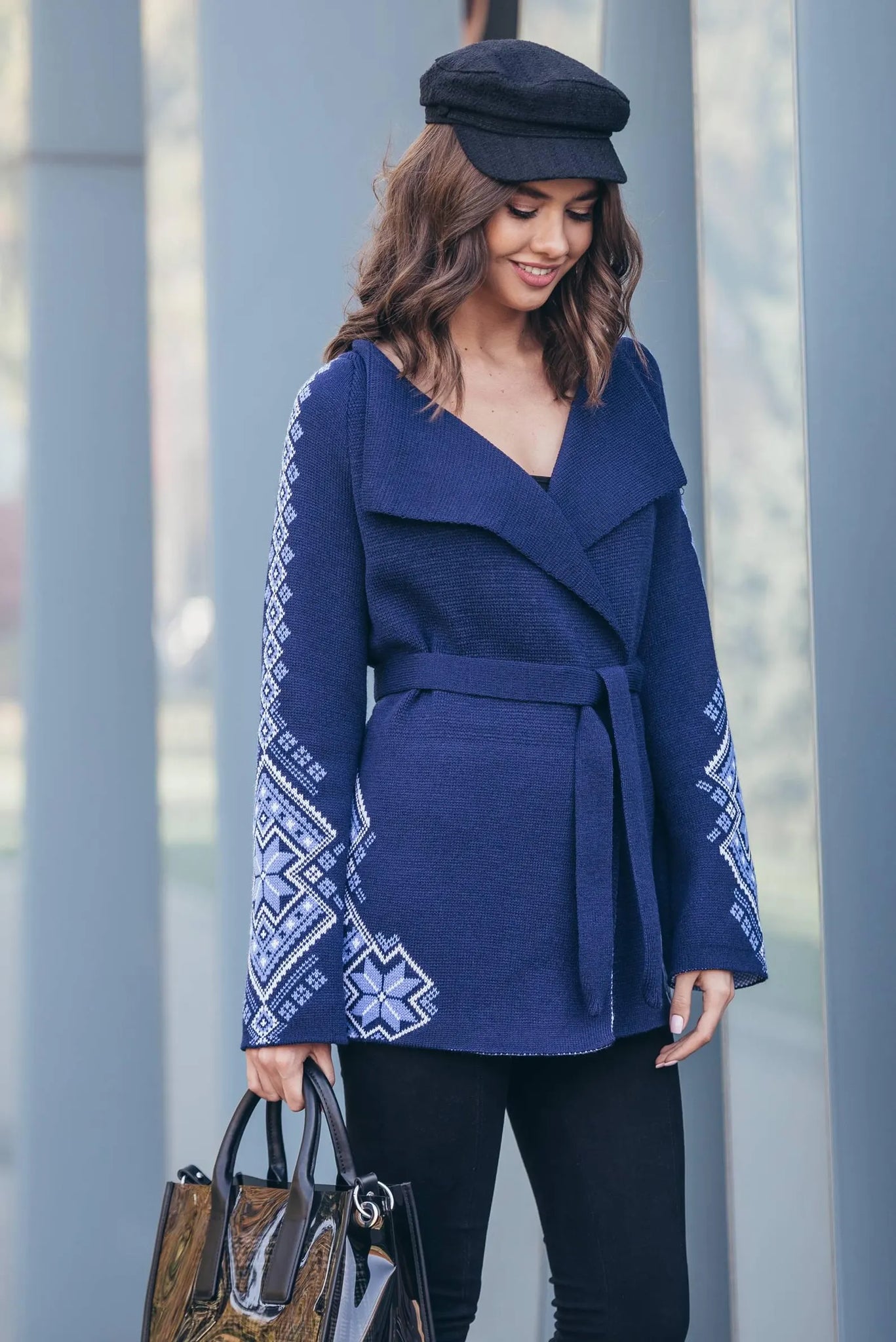 Woman wearing a blue coat with white patterns, holding a handbag, against a gray background.